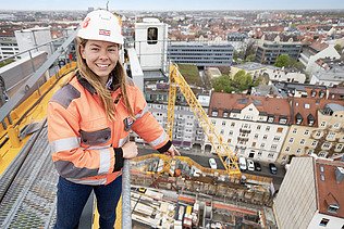 Foto af en byggeleder, der står på en byggekran og peger på byggepladsen
