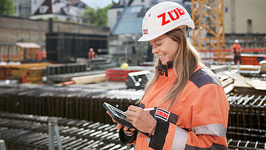 Foto af en byggeleder, der redigerer noget på sin tablet, mens hun står på byggepladsen