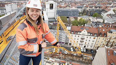 Foto af en byggeleder, der står på en byggekran og peger på byggepladsen