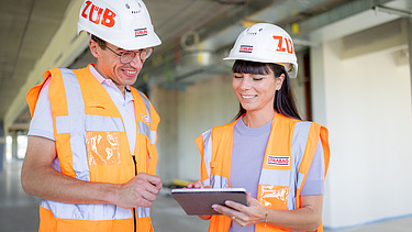 Photo technician standing next to employee with construction helmet pointing